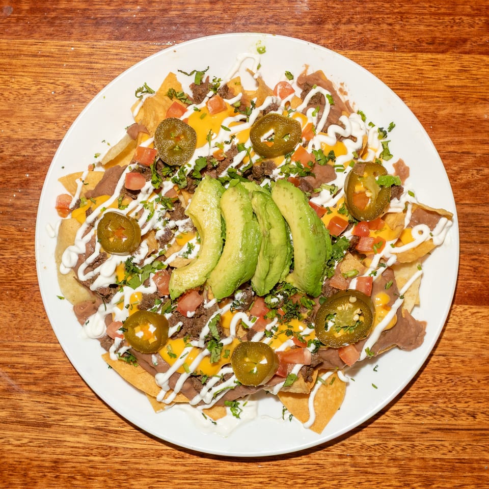 A plate of nachos with cheese, beef, refried beans, avocado, jalapenos, tomatoes, and sour cream.