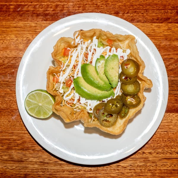 Taco salad in a crispy tortilla bowl with avocado, jalapeños, sour cream, and a lime wedge.