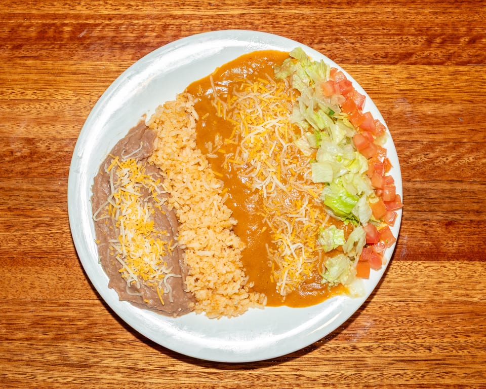 A white plate with refried beans, rice, chili con carne, and a side salad with lettuce and tomatoes.