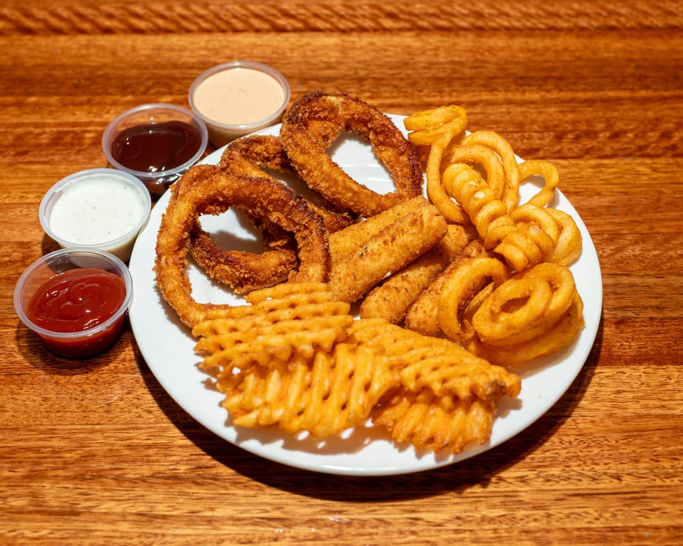 A white plate with fried onion rings, mozzarella sticks, waffle fries, and curly fries, with four dipping sauces.
