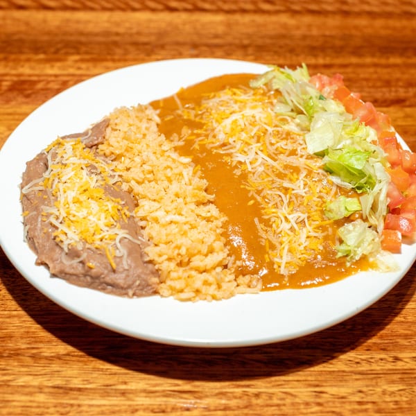A white plate with refried beans, rice, enchilada sauce, shredded cheese, lettuce, and diced tomatoes.