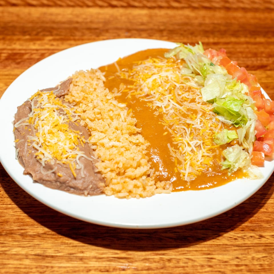 A white plate with refried beans, rice, enchilada sauce, shredded cheese, lettuce, and diced tomatoes.