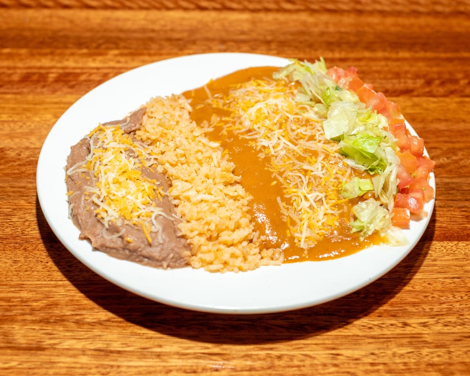 A white plate with refried beans, rice, enchilada sauce, shredded cheese, lettuce, and diced tomatoes.