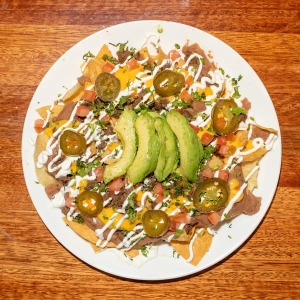 A plate of loaded nachos with beef, cheese, refried beans, avocado, jalapeños, and sour cream.