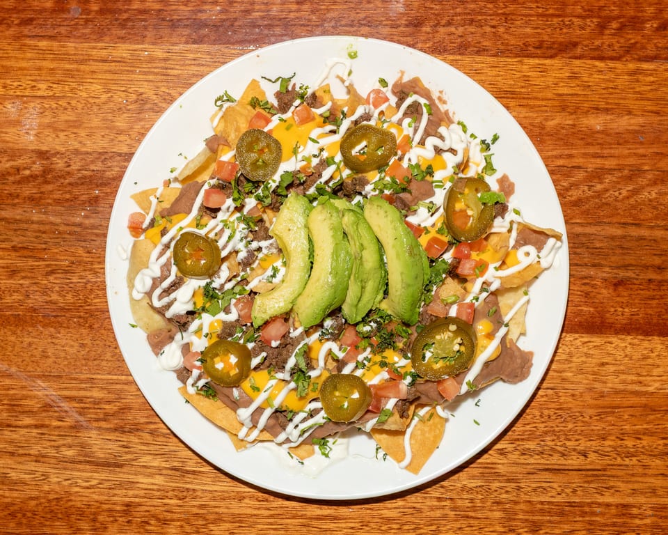 A plate of loaded nachos with beef, cheese, refried beans, avocado, jalapeños, and sour cream.