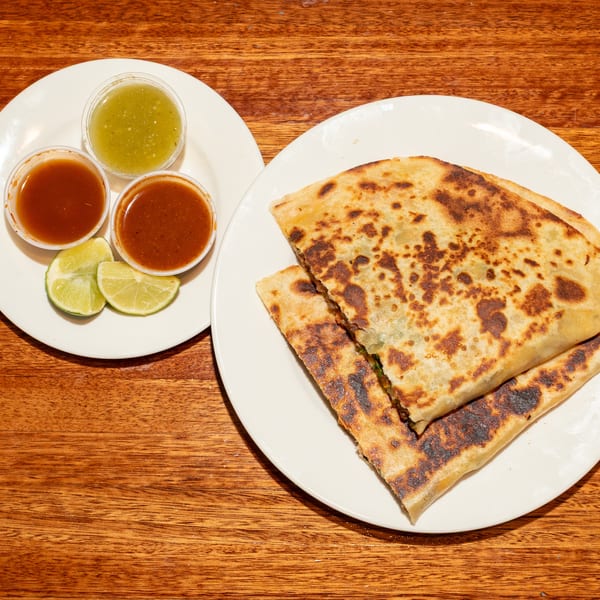 Two plates of food on a wooden table, with quesadillas, salsa, and lime wedges.