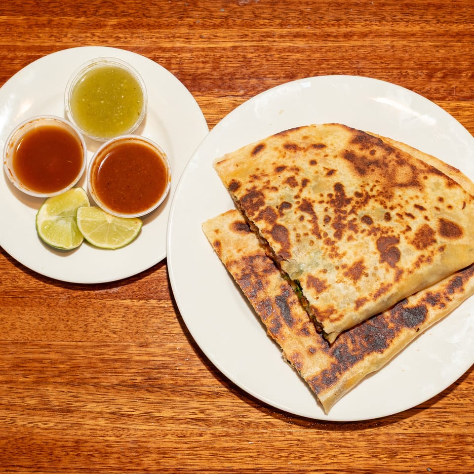Two plates of food on a wooden table, with quesadillas, salsa, and lime wedges.