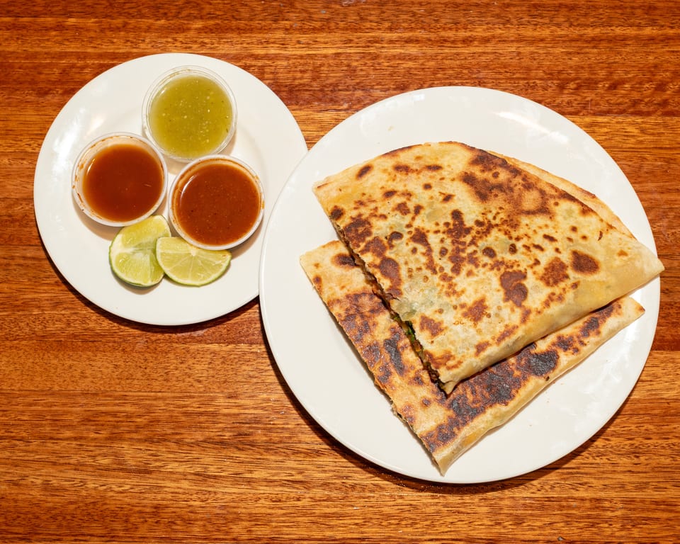 Two plates of food on a wooden table, with quesadillas, salsa, and lime wedges.