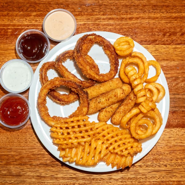 A white plate with onion rings, mozzarella sticks, curly fries, and waffle fries, with four dipping sauces.