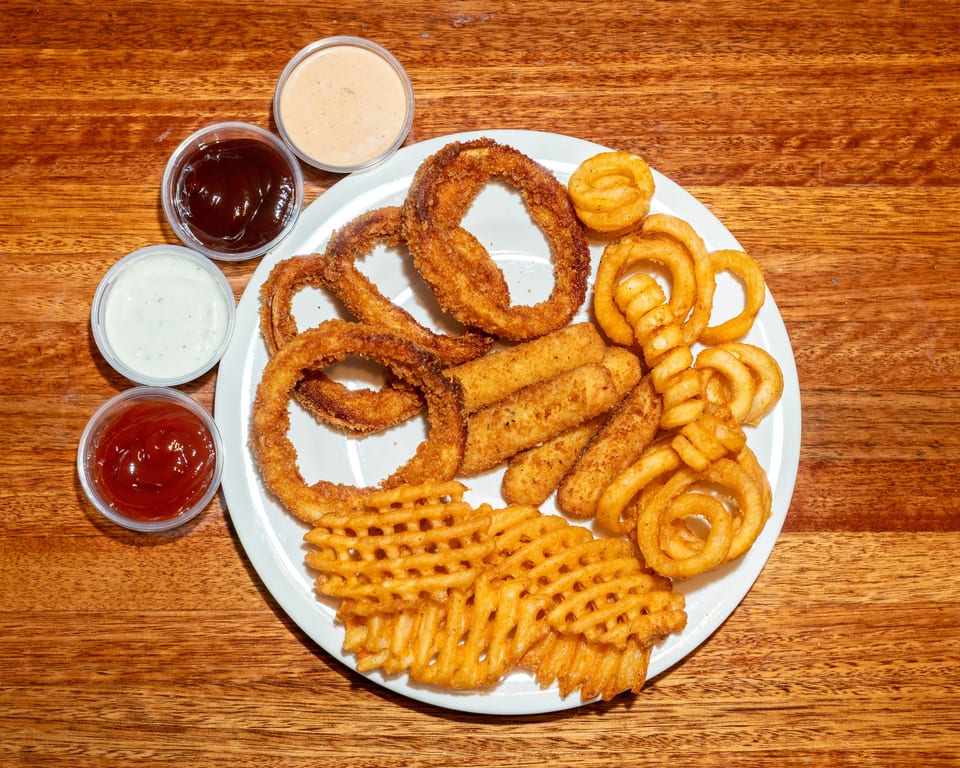 A white plate with onion rings, mozzarella sticks, curly fries, and waffle fries, with four dipping sauces.