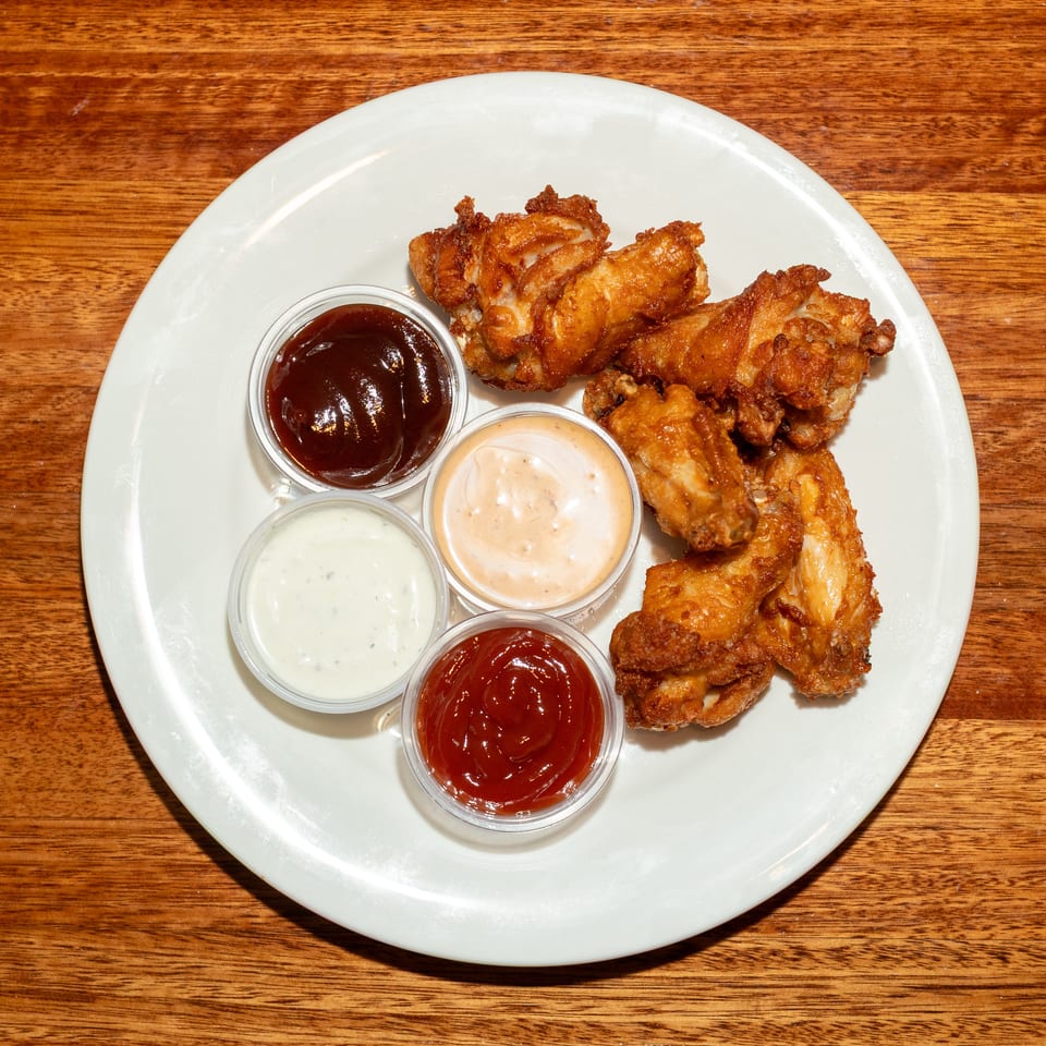 Crispy fried chicken wings with four dipping sauces on a white plate on a wooden table.