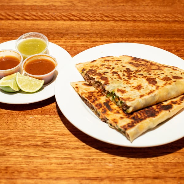 Two plates of quesadillas, salsas, and lime wedges on a wooden table.