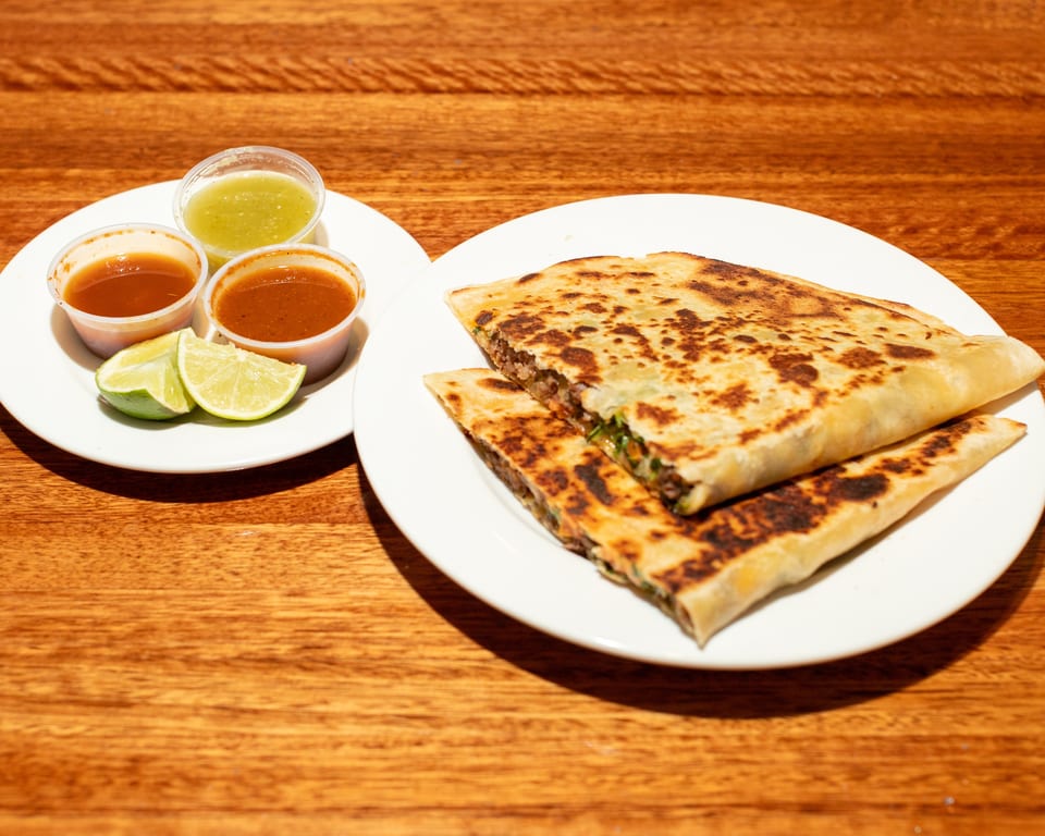 Two plates of quesadillas, salsas, and lime wedges on a wooden table.