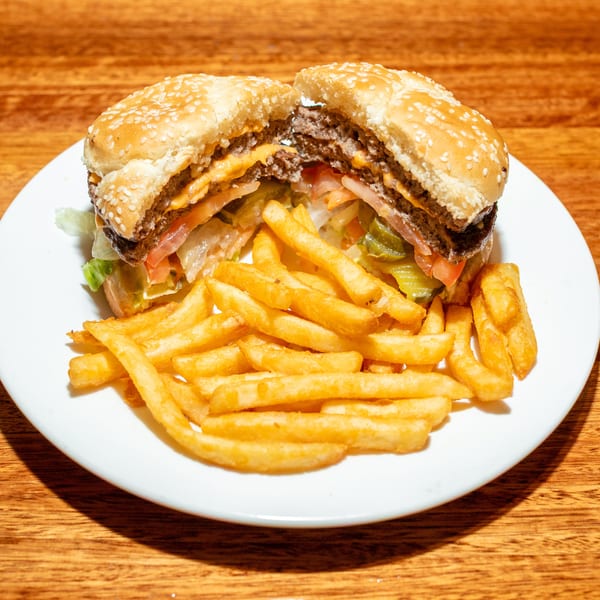 A double cheeseburger, cut in half, with lettuce, tomato, and pickles, served with fries.