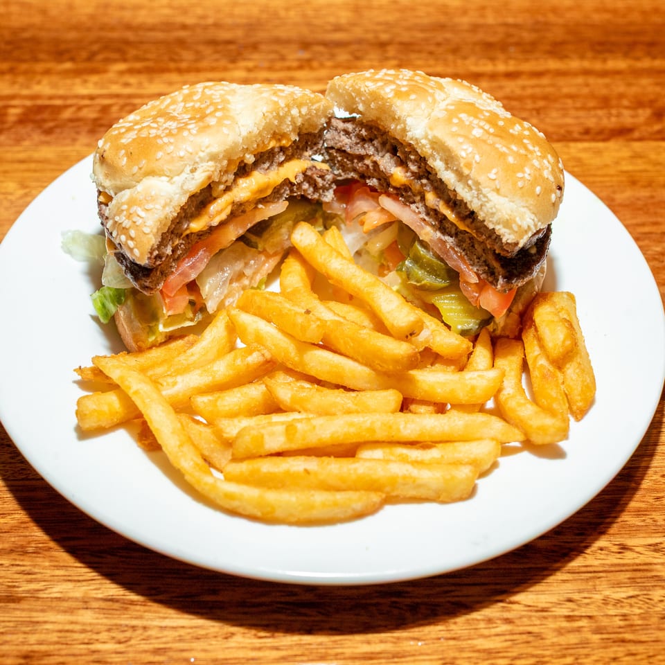 A double cheeseburger, cut in half, with lettuce, tomato, and pickles, served with fries.