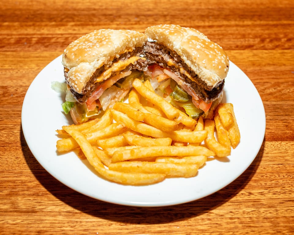 A double cheeseburger, cut in half, with lettuce, tomato, and pickles, served with fries.