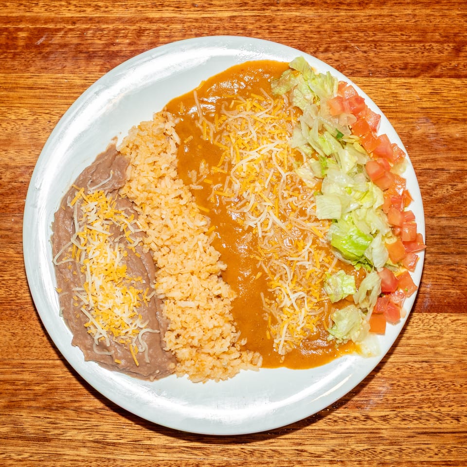 A white plate with refried beans, rice, chili con carne, shredded lettuce, and diced tomatoes.