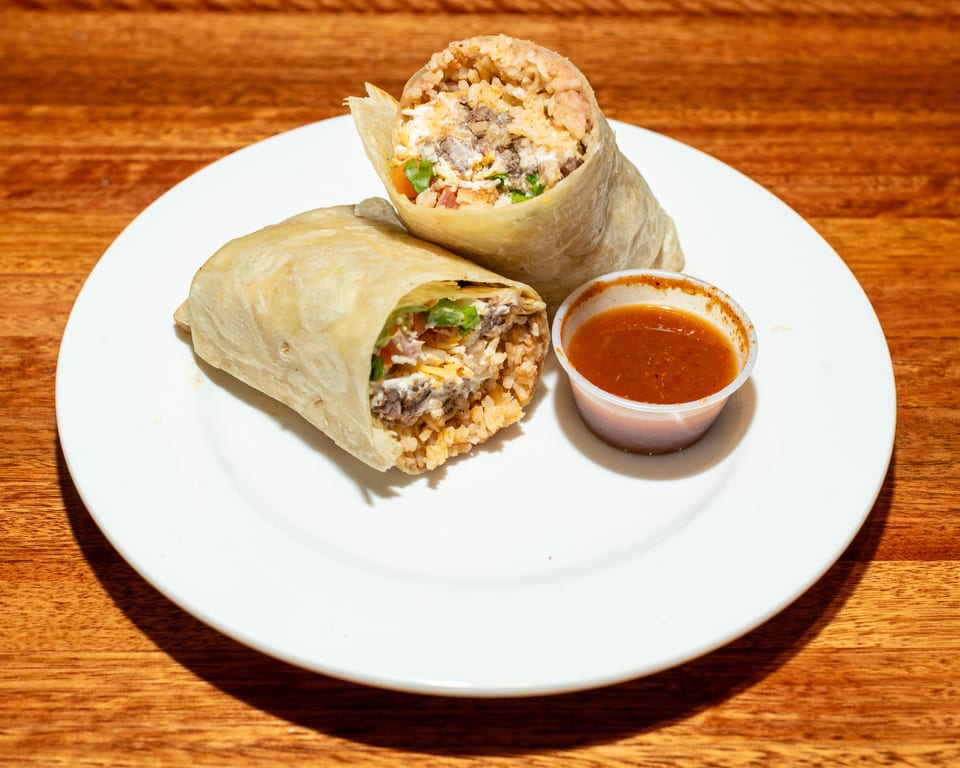 Two burritos, one cut open to show rice, meat, cheese, and vegetables, with a side of salsa.