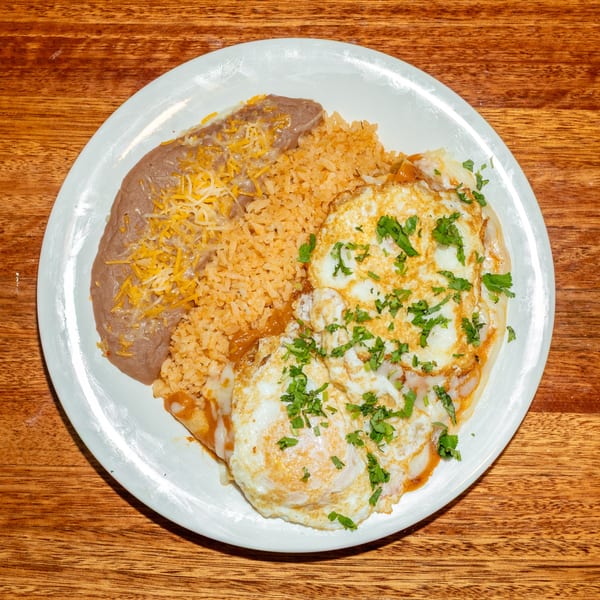 A white plate with huevos rancheros, refried beans topped with cheese, and Spanish rice.