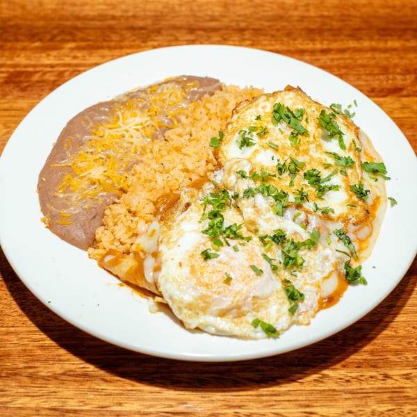 A plate of huevos rancheros with refried beans, rice, and two fried eggs topped with cilantro.