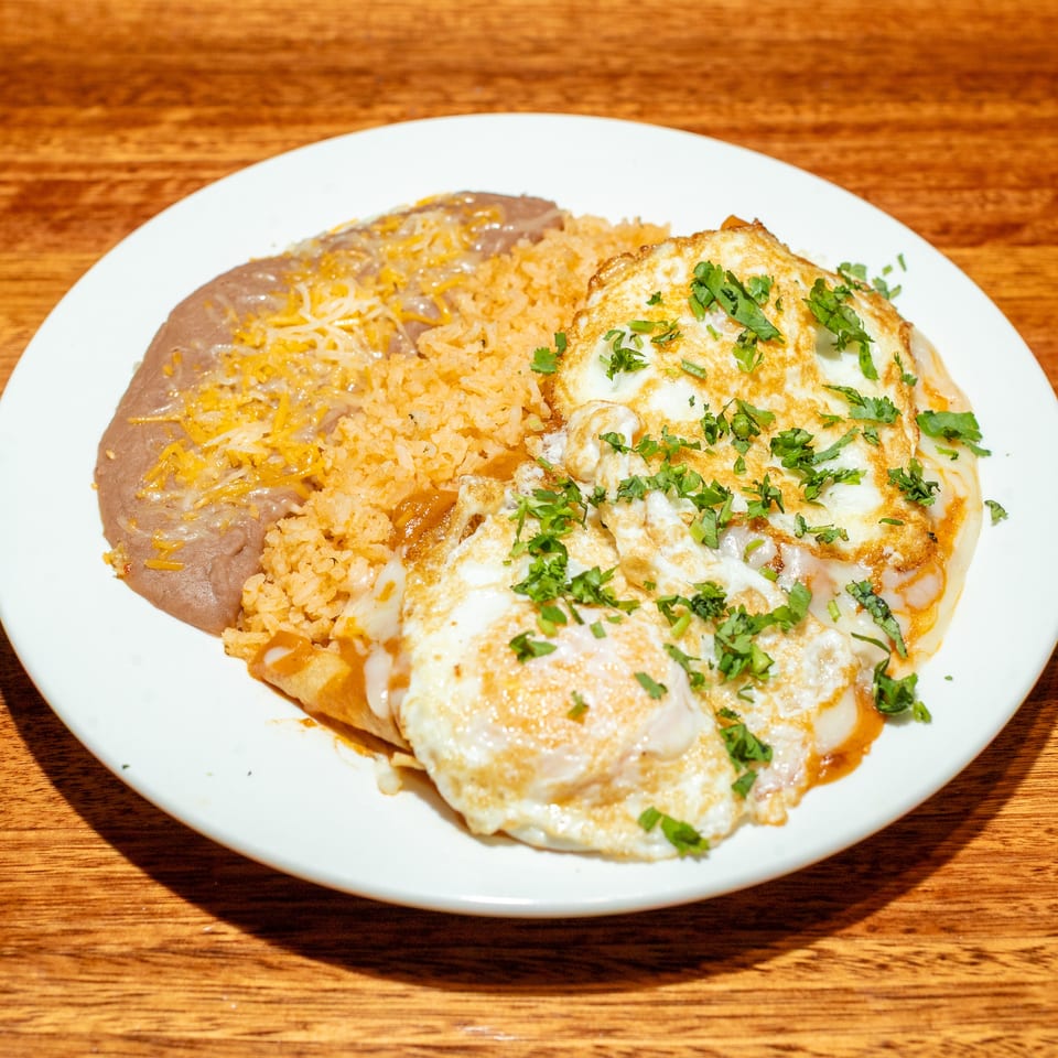 A plate of huevos rancheros with refried beans, rice, and two fried eggs topped with cilantro.