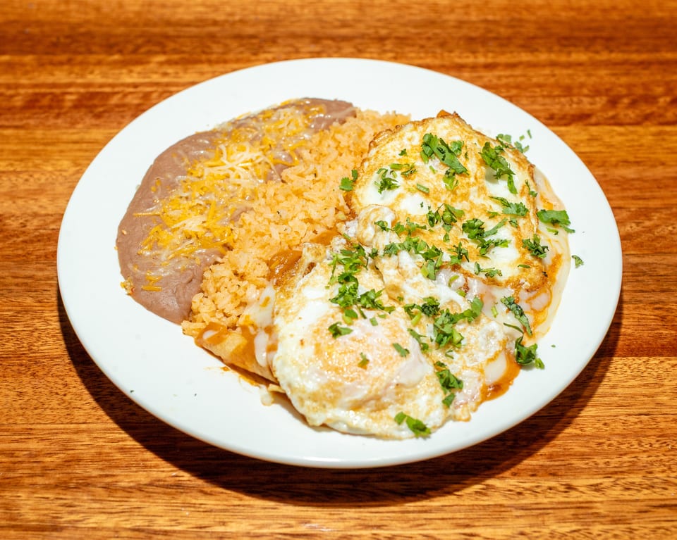 A plate of huevos rancheros with refried beans, rice, and two fried eggs topped with cilantro.