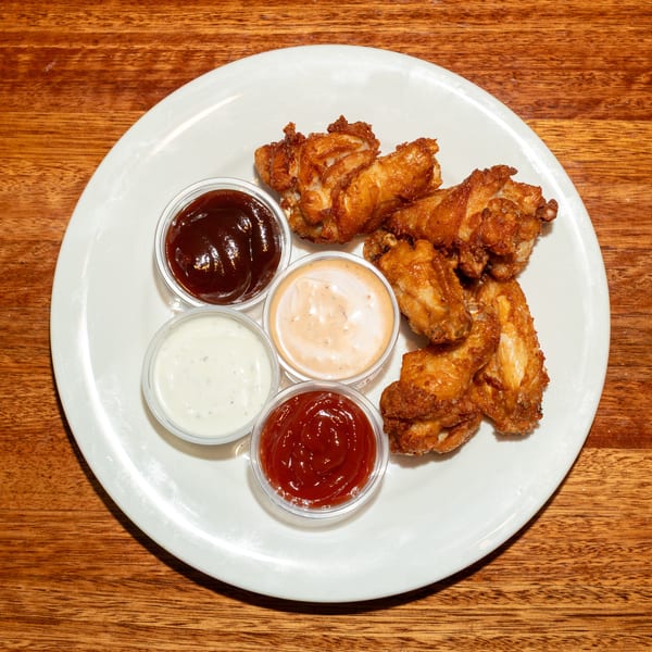 Crispy fried chicken wings with four dipping sauces on a white plate on a wooden table.