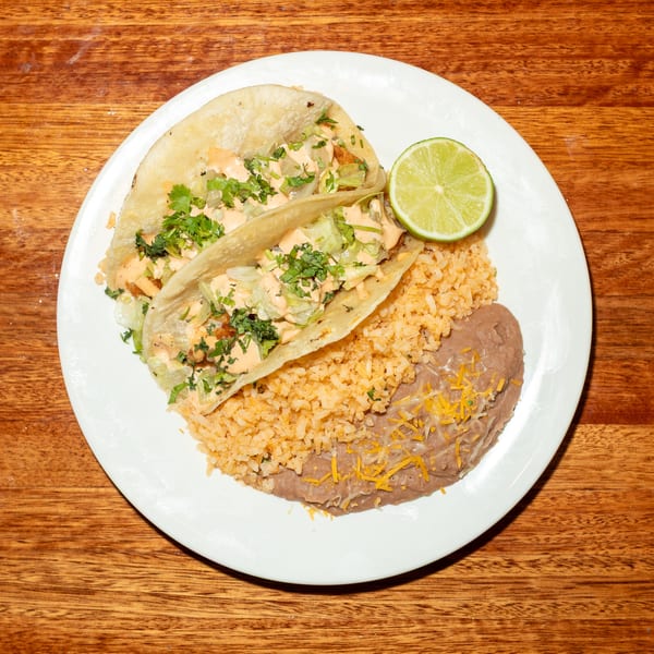 Two fish tacos with rice, refried beans, and a lime wedge on a white plate.