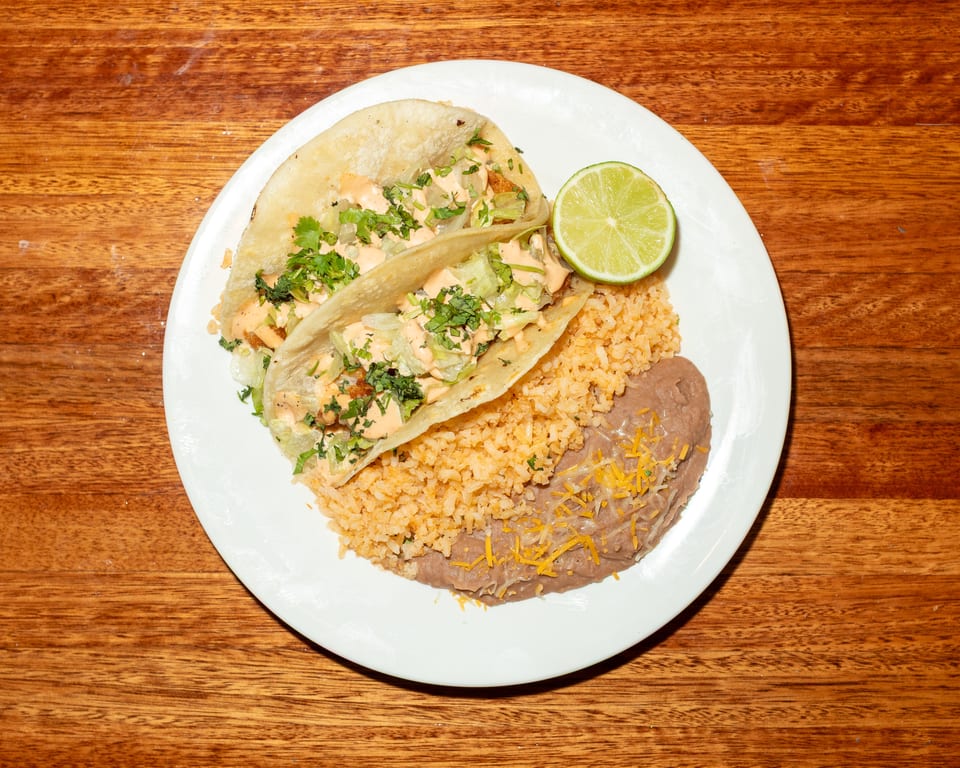 Two fish tacos with rice, refried beans, and a lime wedge on a white plate.