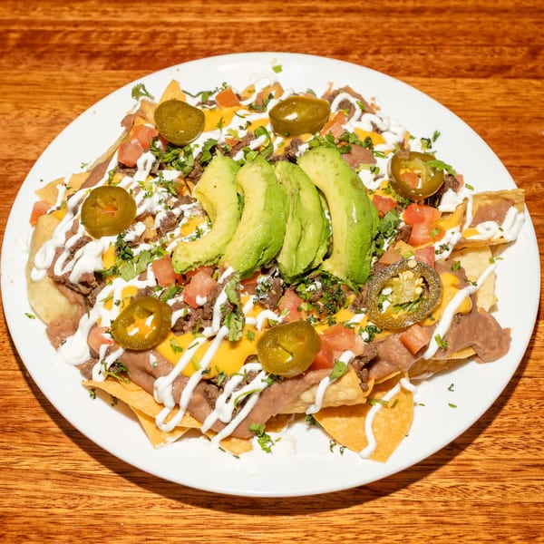 Loaded nachos with beef, refried beans, cheese, avocado, jalapeños, tomatoes, and sour cream.