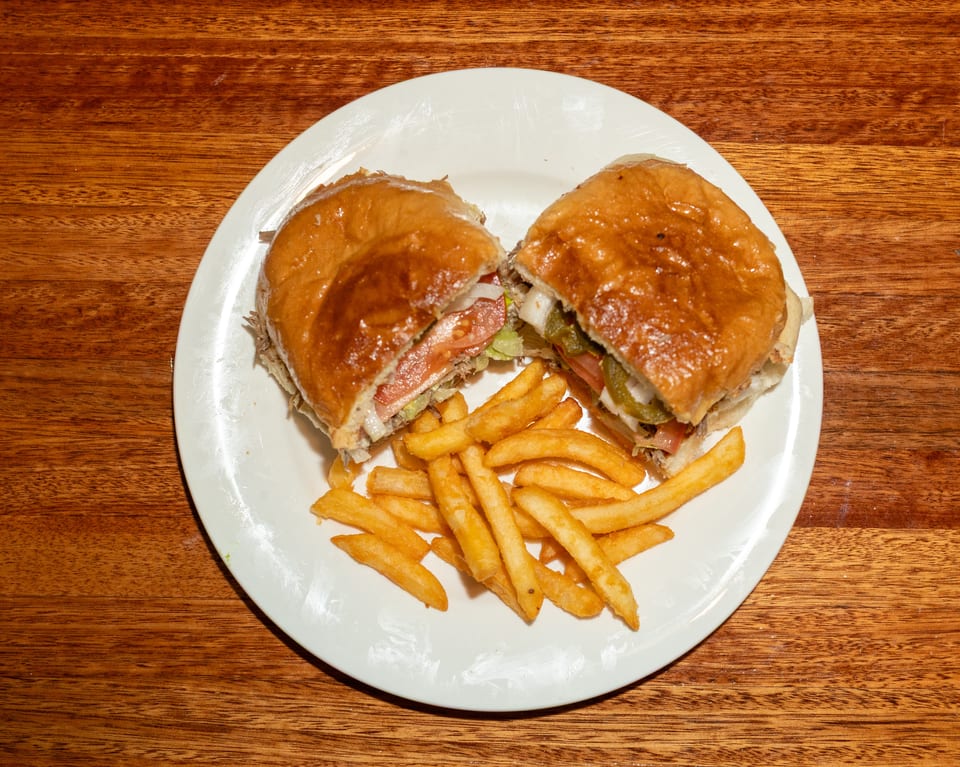 A large sandwich cut in half, revealing meat, lettuce, tomato, and onions, served with fries.