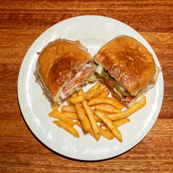 A large sandwich cut in half, revealing meat, lettuce, tomato, onions, and peppers, served with fries.