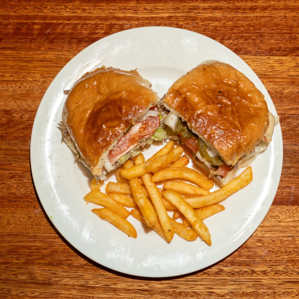 A large sandwich cut in half, revealing meat, lettuce, tomato, onions, and peppers, served with fries.